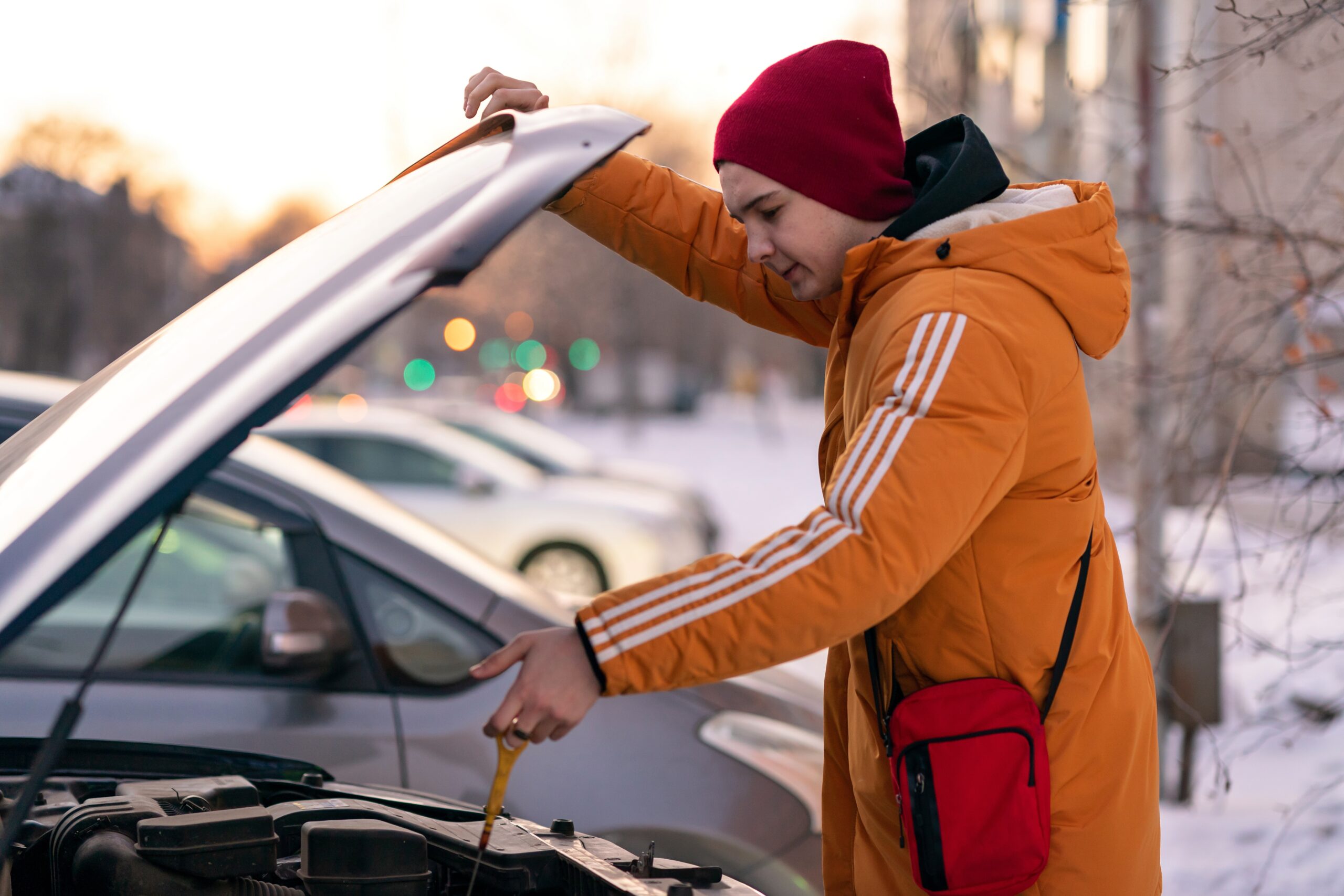 A young man wearing a yellow jacket checks the oil level of a car using a dipstick.