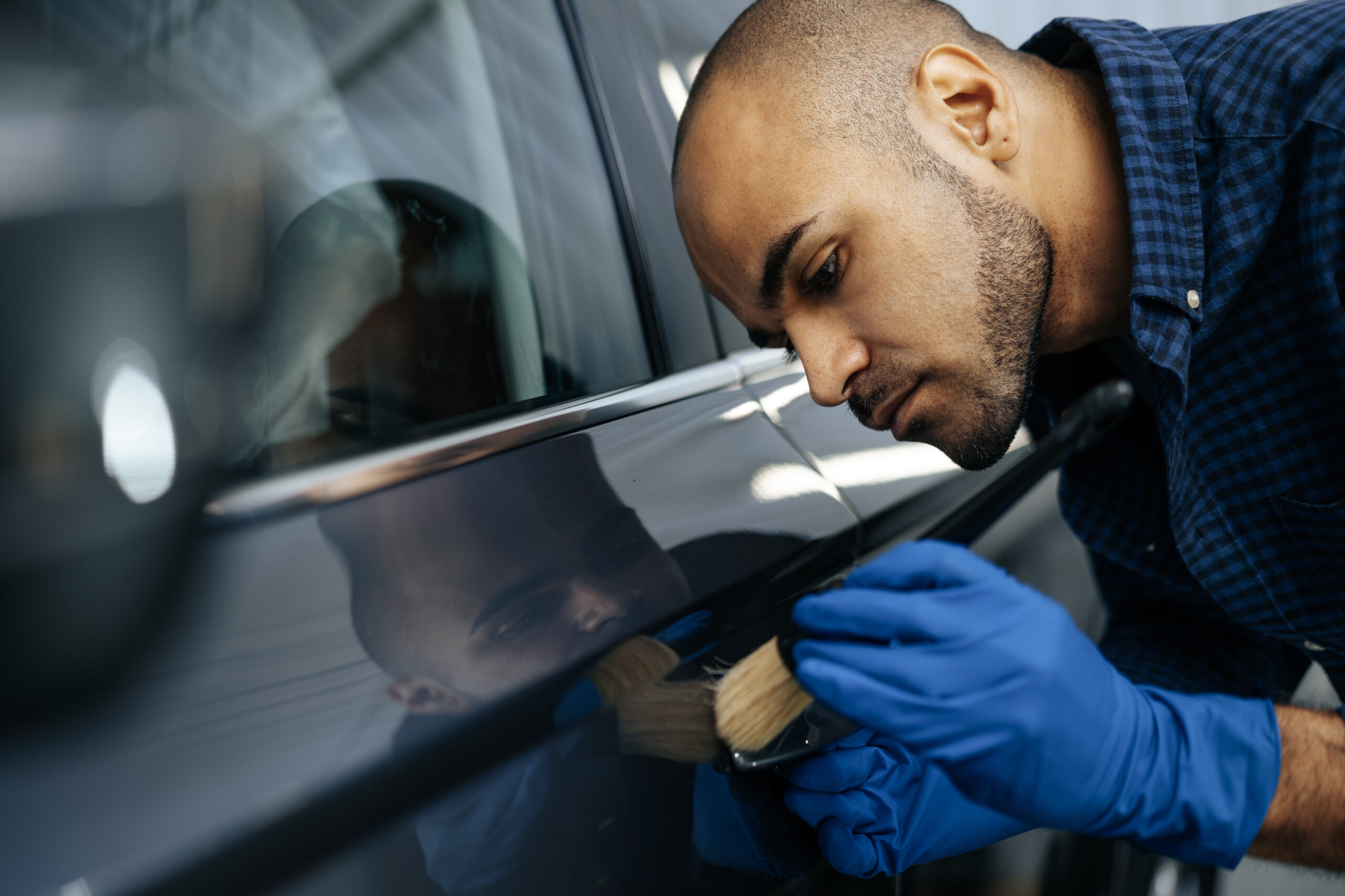 A skilled African American car detailer meticulously applies nano ceramic coating to a vehicle's hood, ensuring a glossy finish and long-lasting protection.