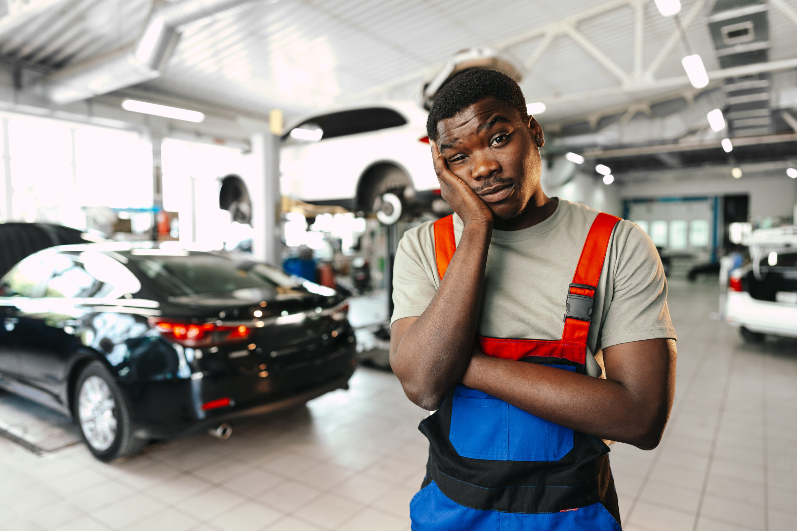 A skilled African man mechanic in uniform meticulously working on a car in a professional repair station.