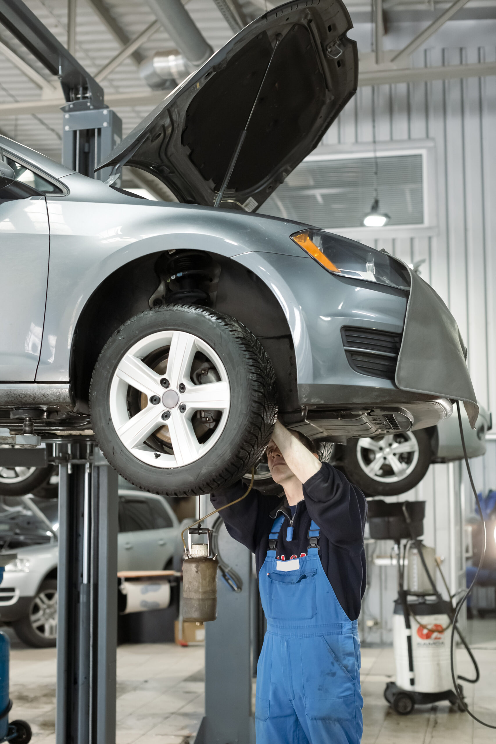 A car raised on a hydraulic lift in a brightly lit auto repair shop, showcasing the vehicle's undercarriage for maintenance and repair.