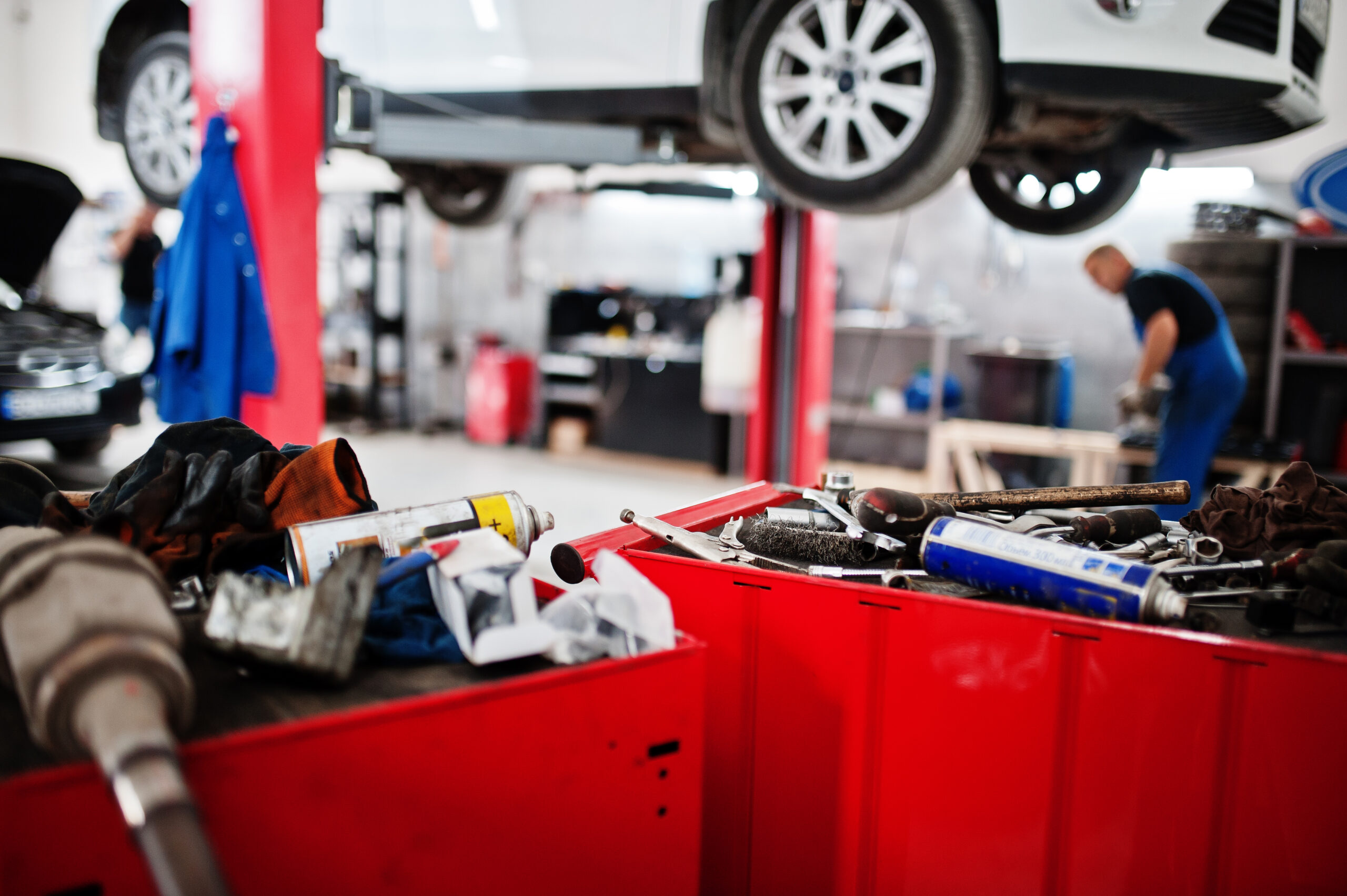 A car being lifted on a hydraulic lift in a car repair shop.