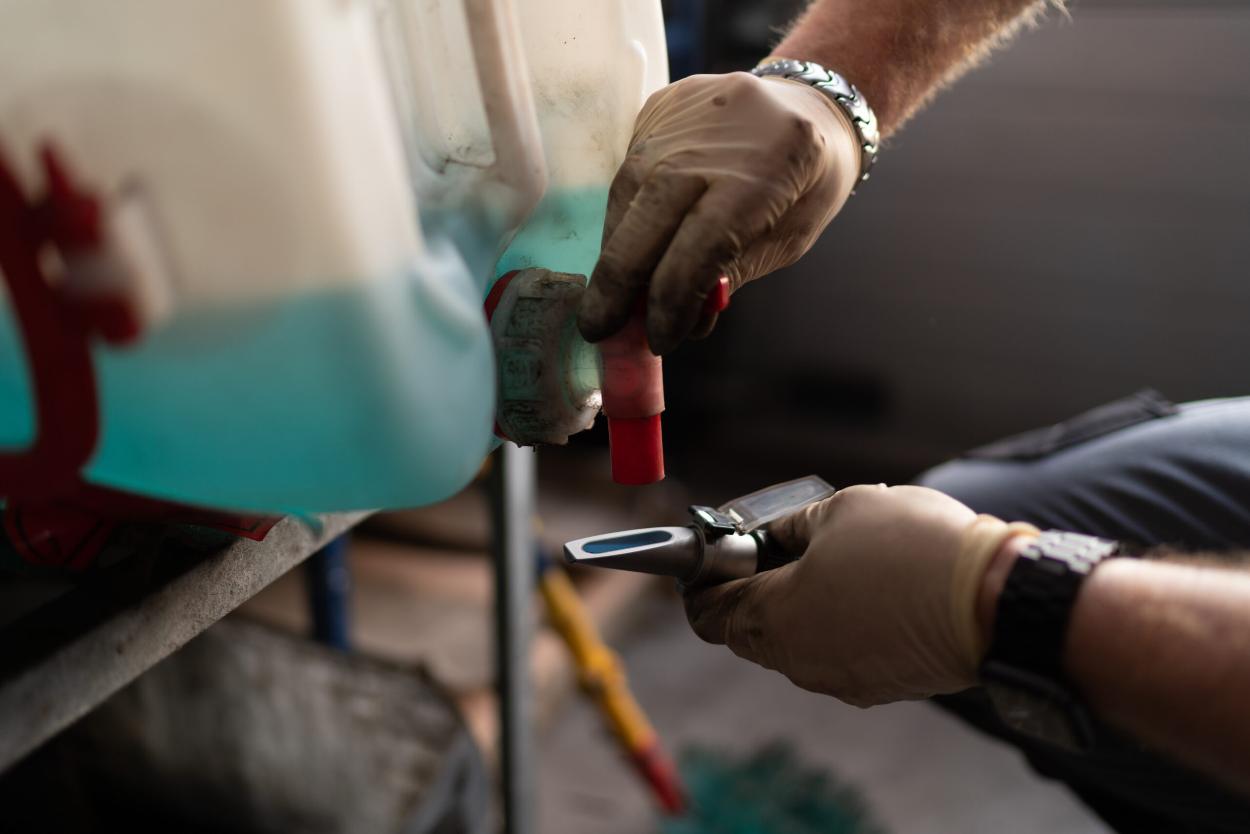 car service technician in a blue uniform leans over the engine compartment, carefully checking the windshield washer fluid level.