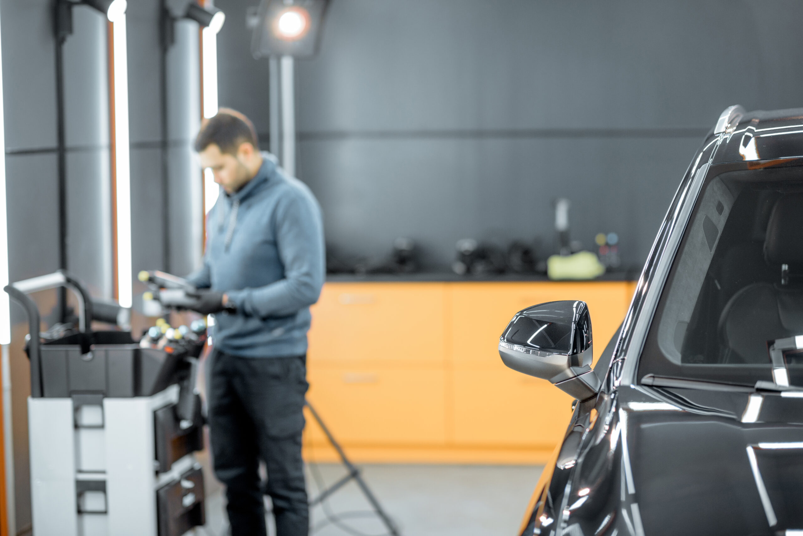 A car service worker in a well-equipped garage, carefully inspecting a car's paintwork before detailing.