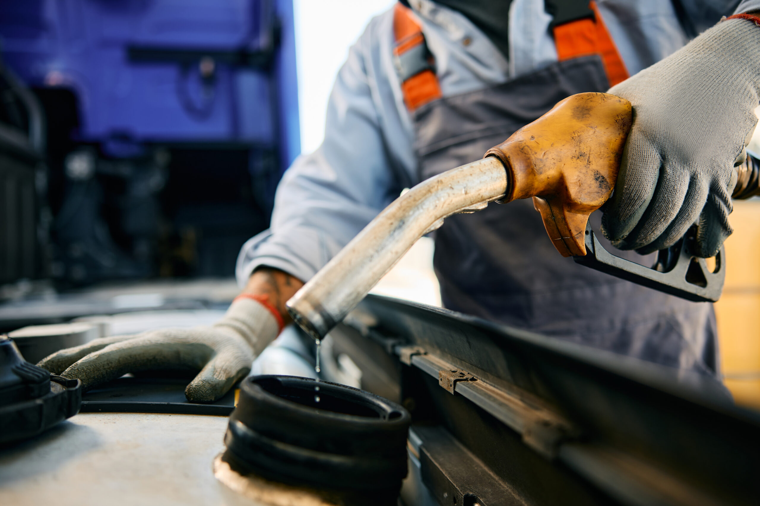 A close-up of a hand holding a gas pump nozzle, filling a car's fuel tank with gasoline.