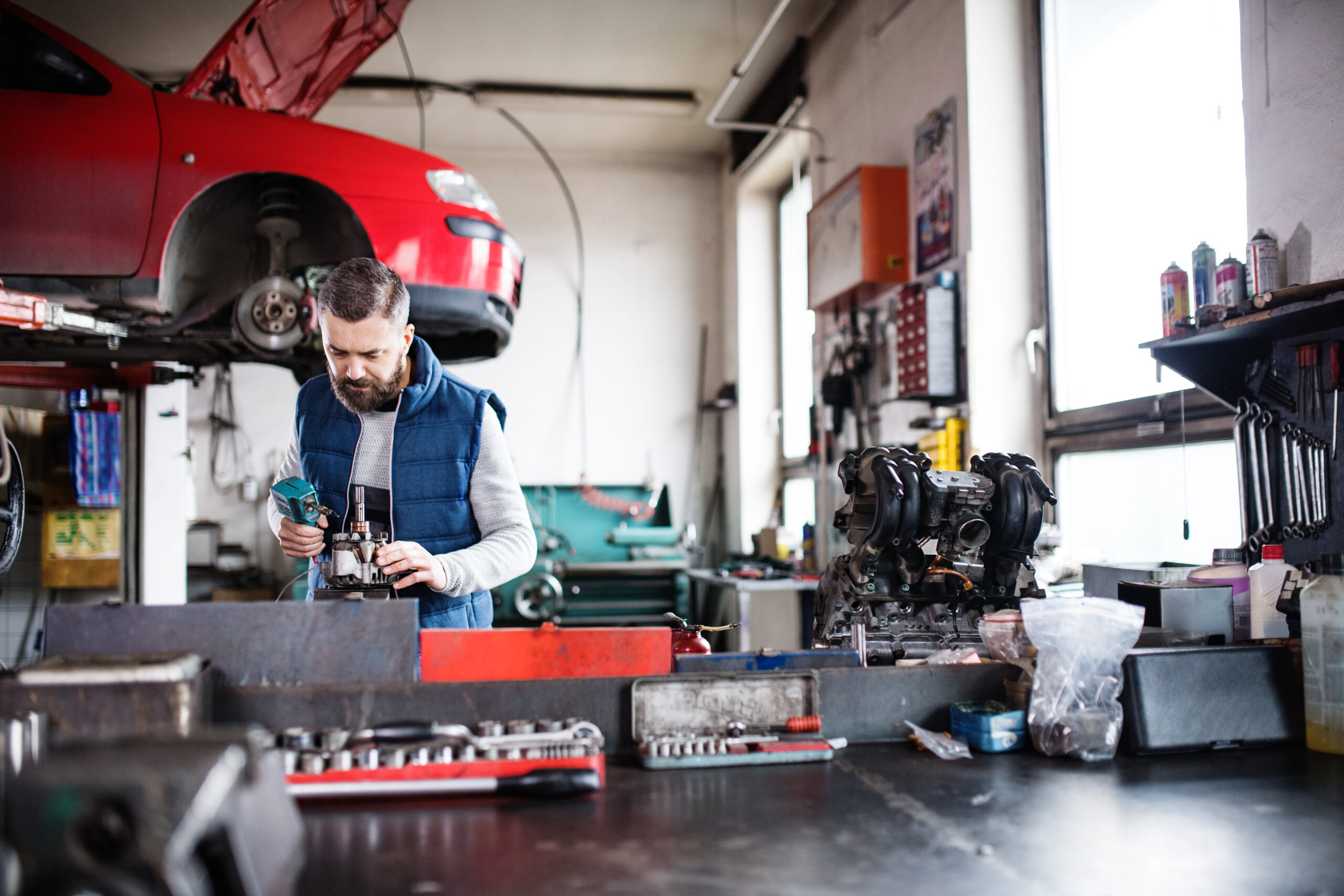 A mechanic in coveralls lies under a car on a creeper, using a wrench to tighten a bolt