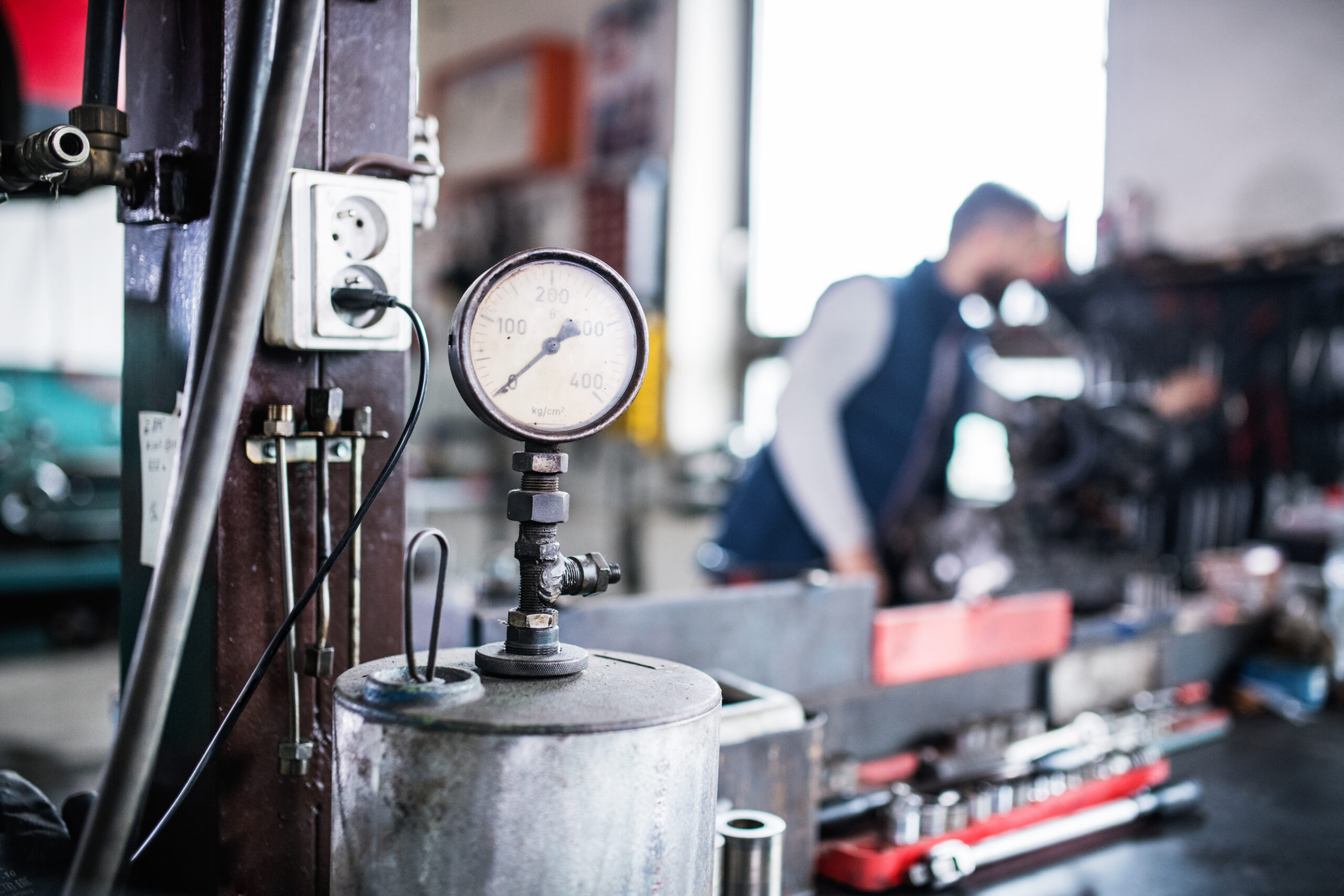 A mechanic in coveralls lies under a car on a creeper, using a wrench to tighten a bolt.