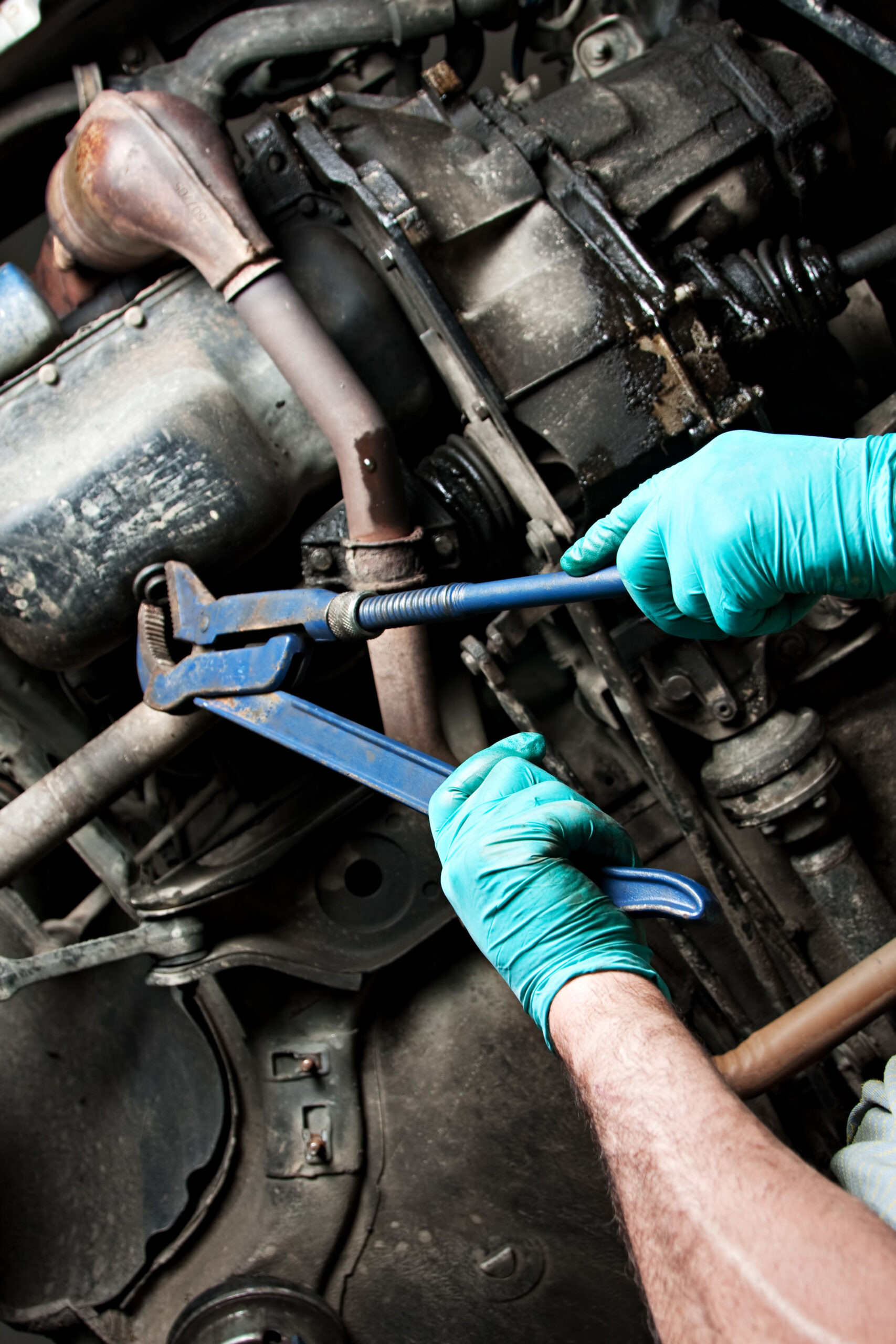 A mechanic in a blue jumpsuit works on a car engine in a brightly lit auto repair shop.