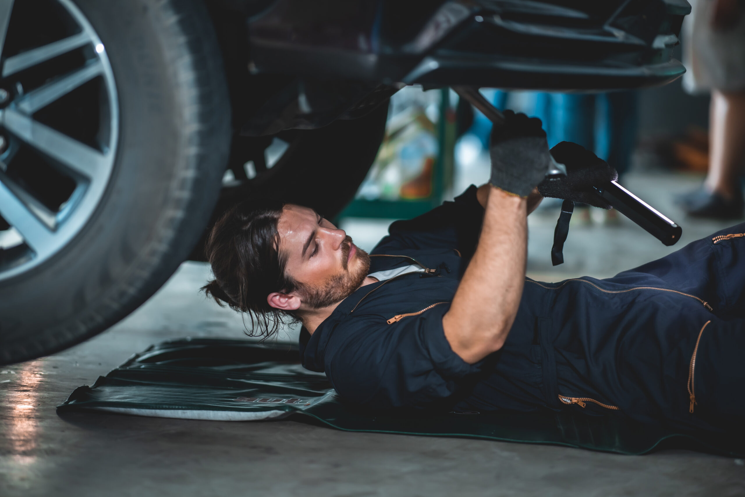 A mechanic in coveralls using a wrench to tighten a bolt on a car engine.