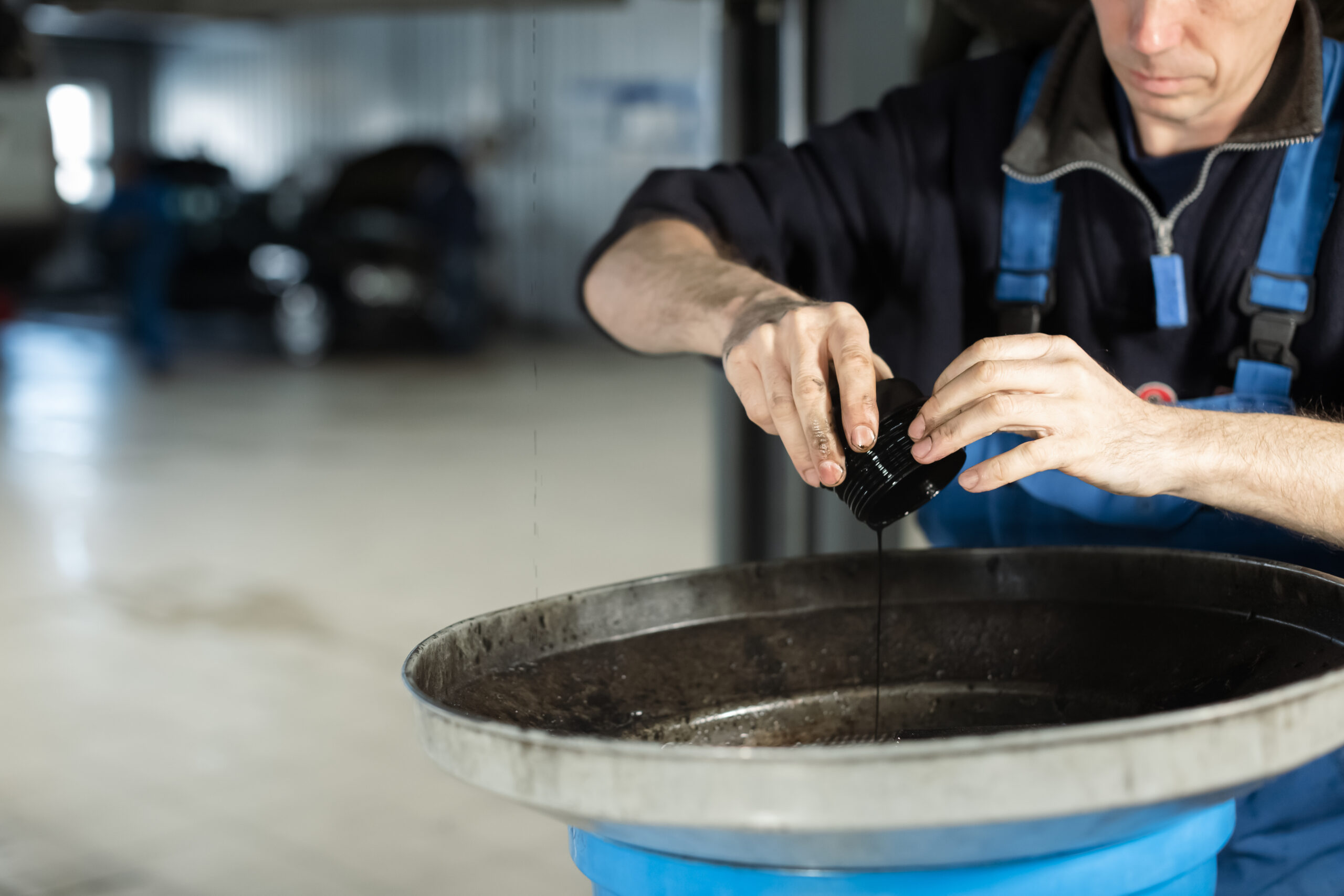 A mechanic in a blue uniform carefully replaces a car's oil filter as part of a routine maintenance service.