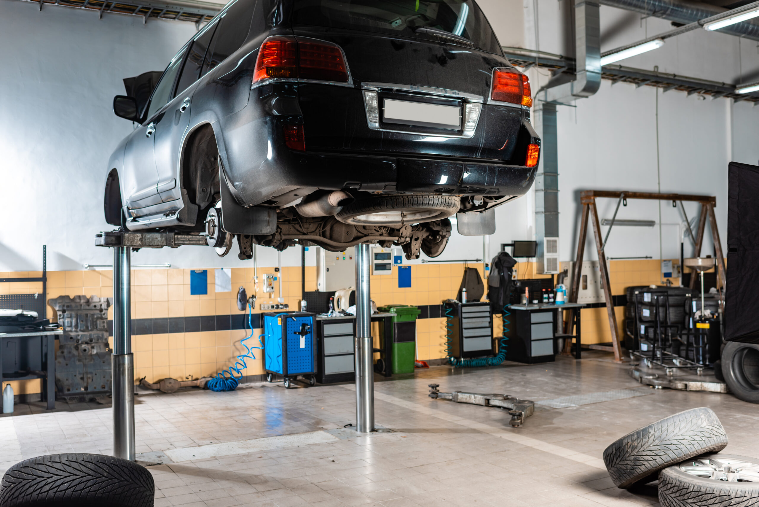 A sleek black car hoisted on a hydraulic lift in a well-lit auto repair shop.