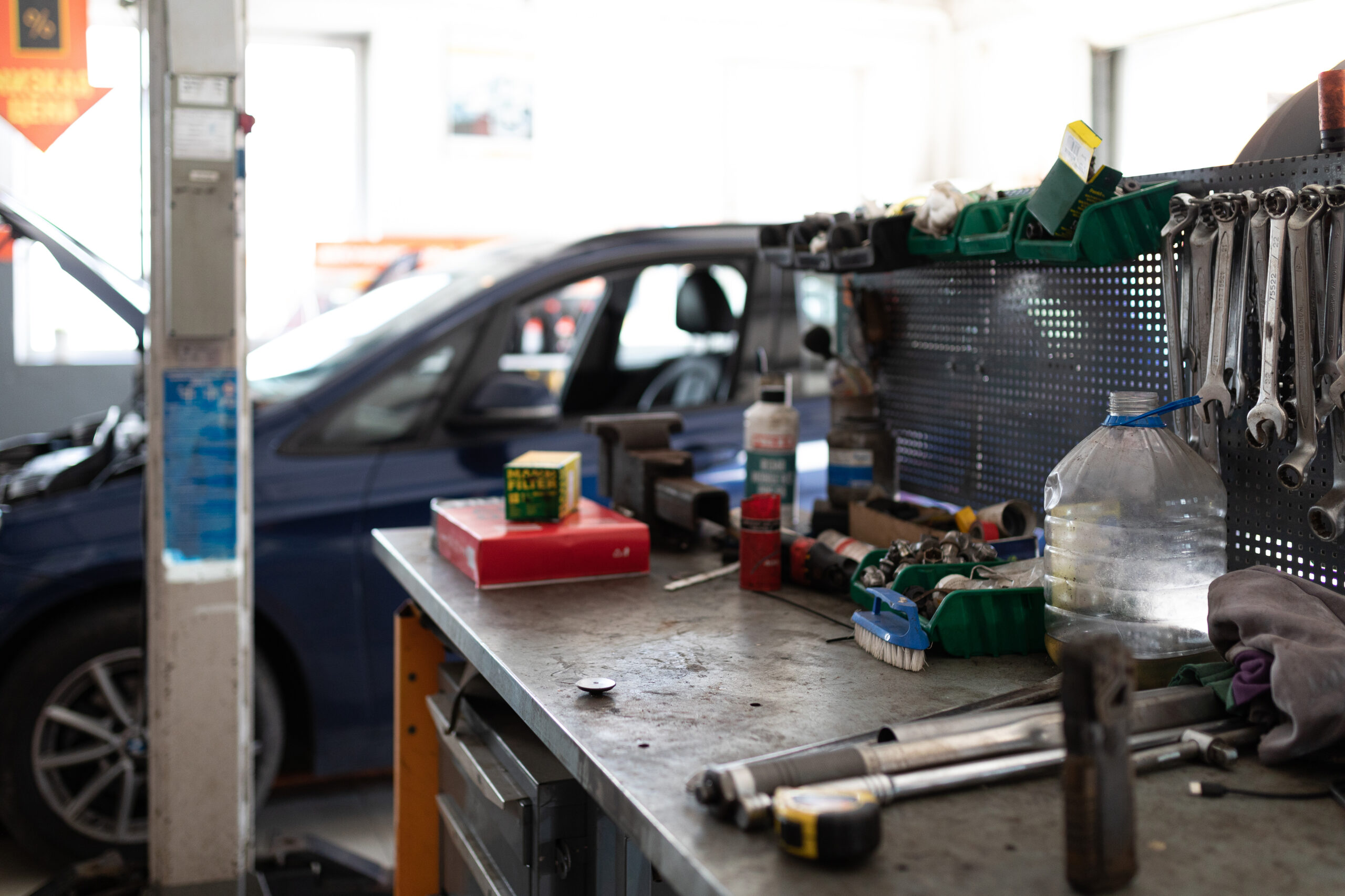 A metal workbench covered in tools, with a blue car undergoing repairs in the background.