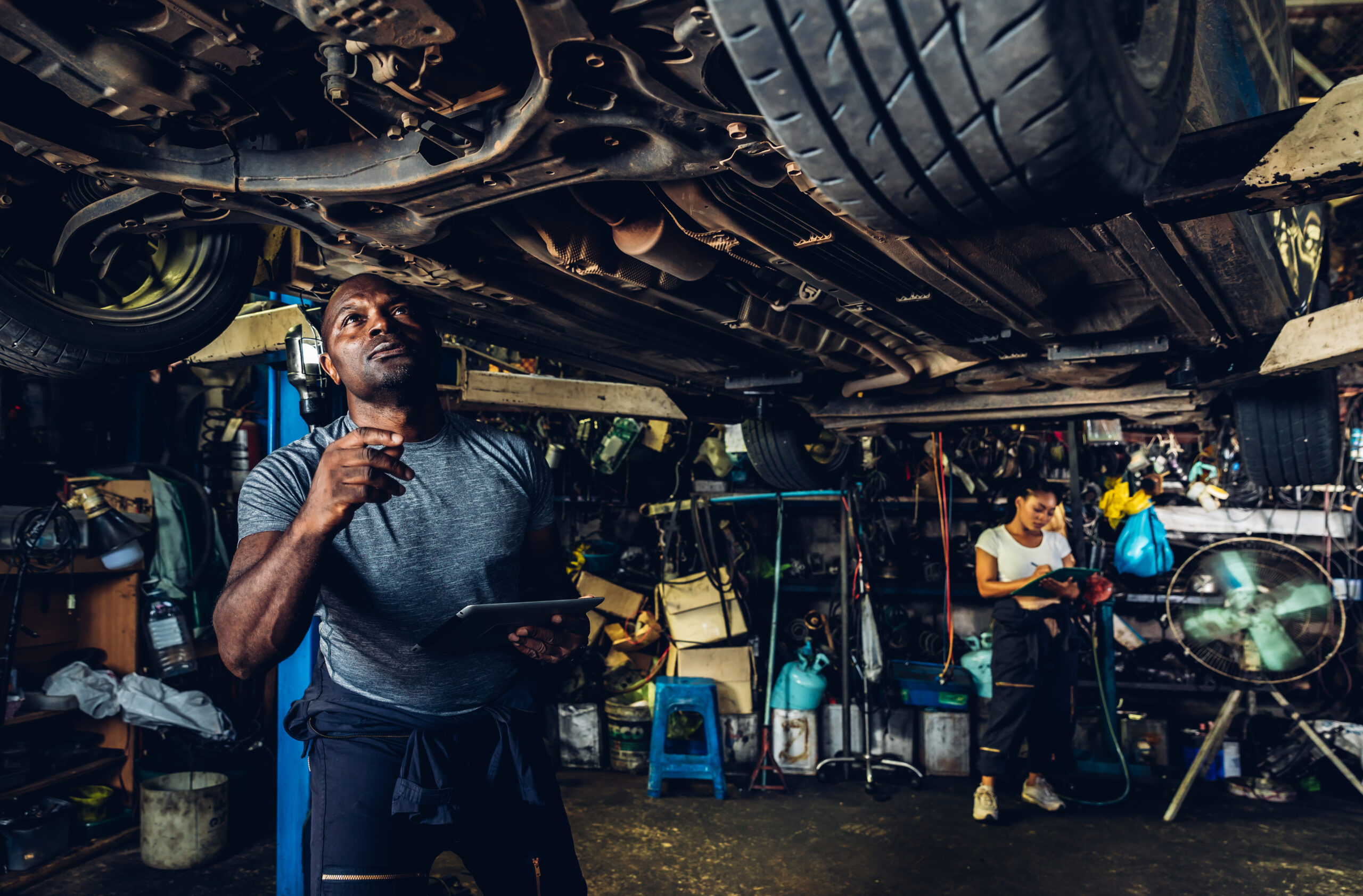 Car mechanic wearing safety glasses and gloves, lying on a creeper and inspecting the underside of a car.