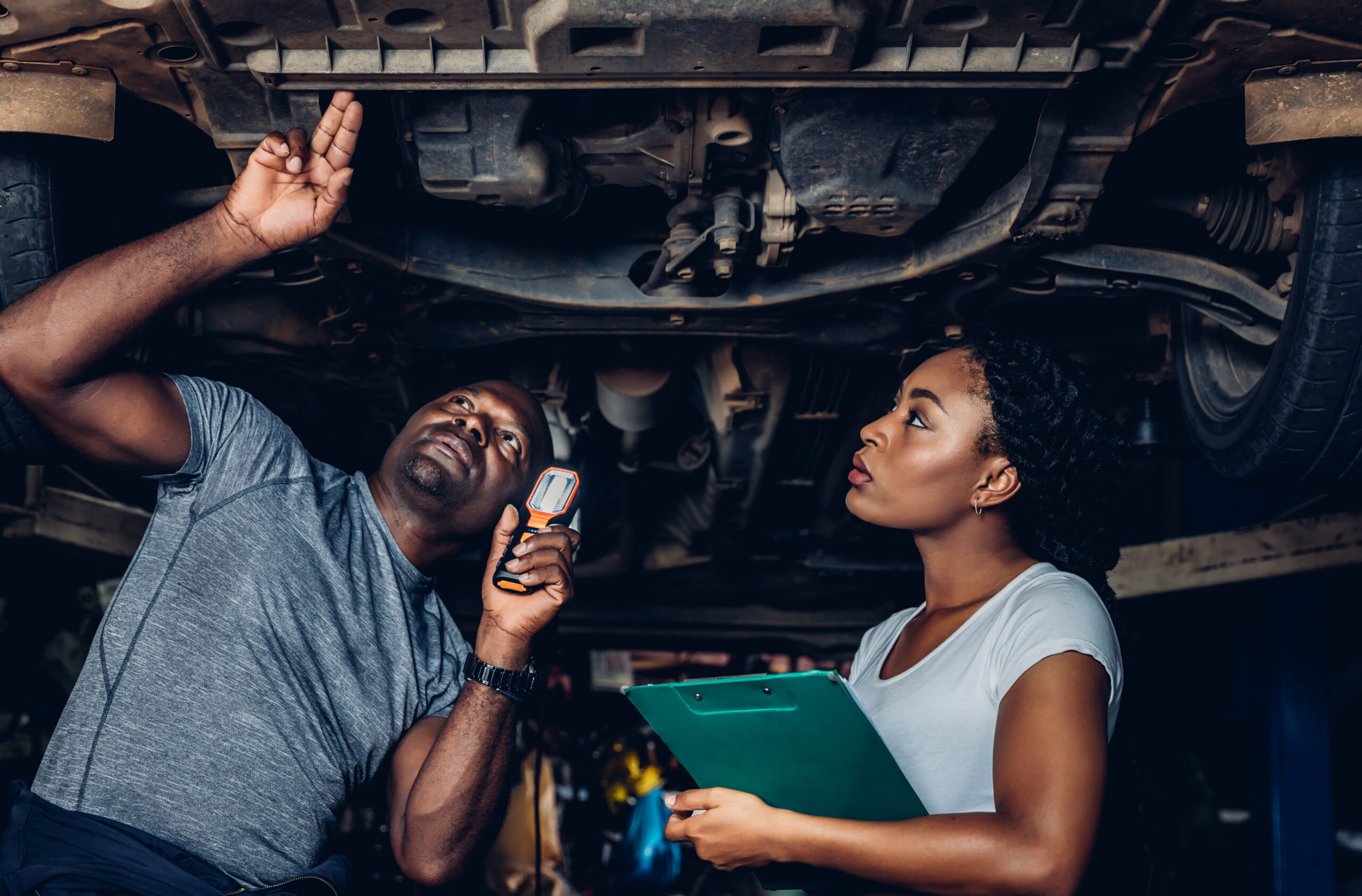 A young woman, looking confused, stands beside her car with the hood open, examining the engine on a city street.