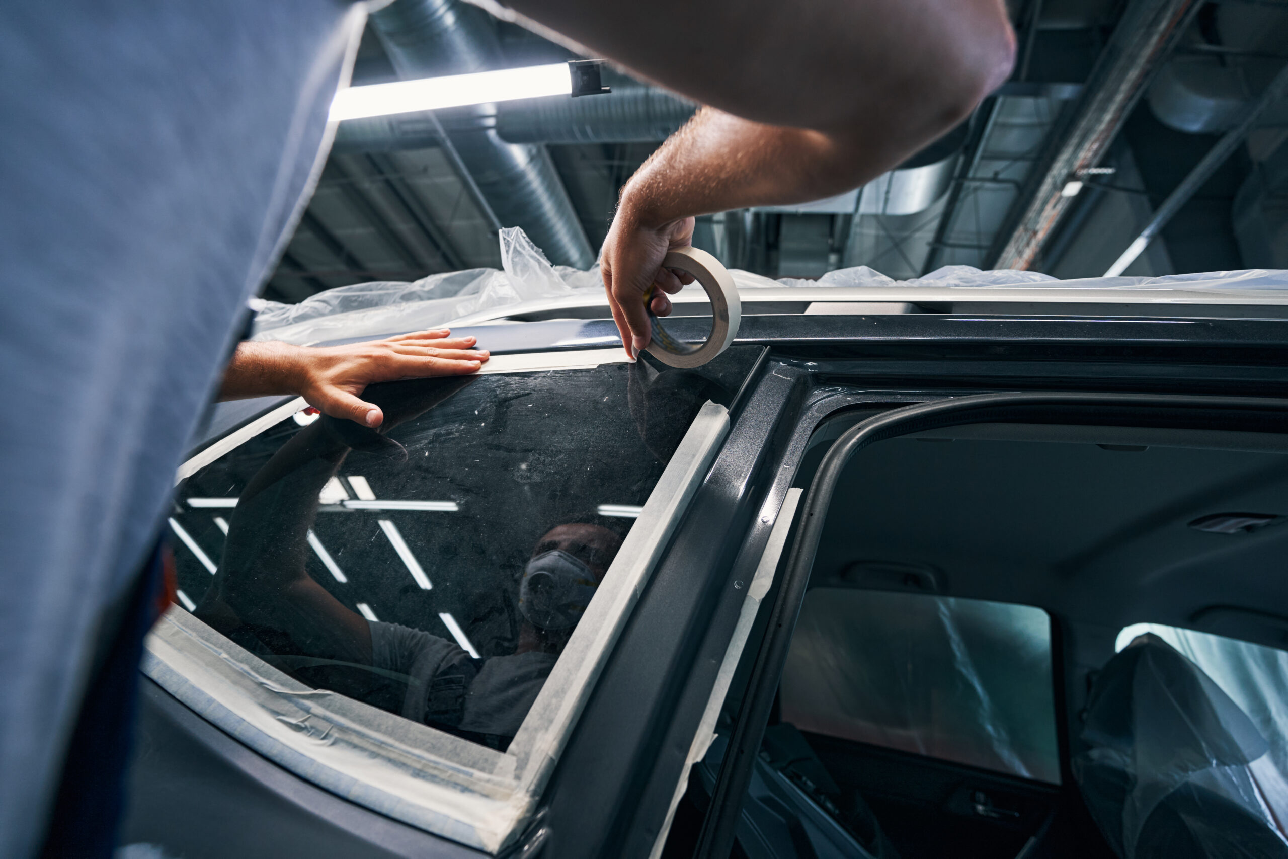 A repairman carefully applies insulating tape around a car window, ensuring a tight seal and improved energy efficiency.